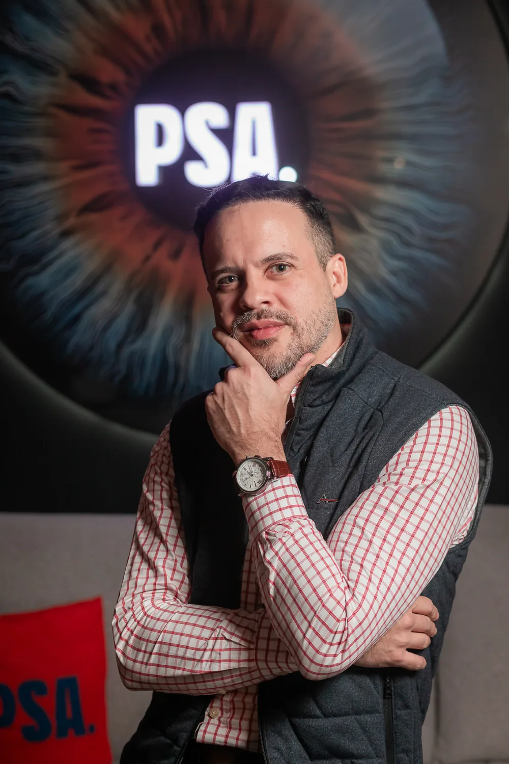 Retrato de Gabriel Pavão com a mão no queixo, em pose reflexiva, em ambiente de estúdio.